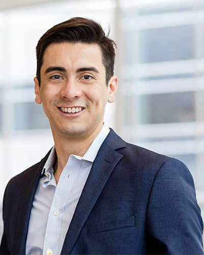 Un professionnel souriant, vêtu d'un costume sombre, se tient dans un environnement moderne et lumineux, rayonnant de confiance.