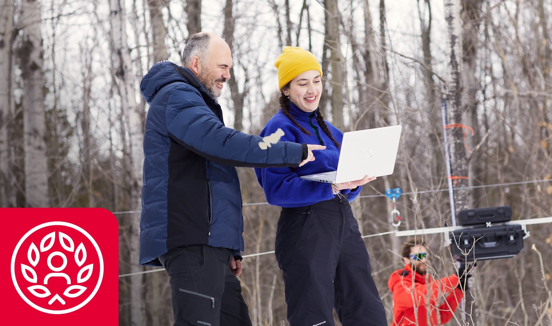Deux personnes échangent des idées en pleine nature, utilisant un ordinateur portable, entourées d'un paysage hivernal.