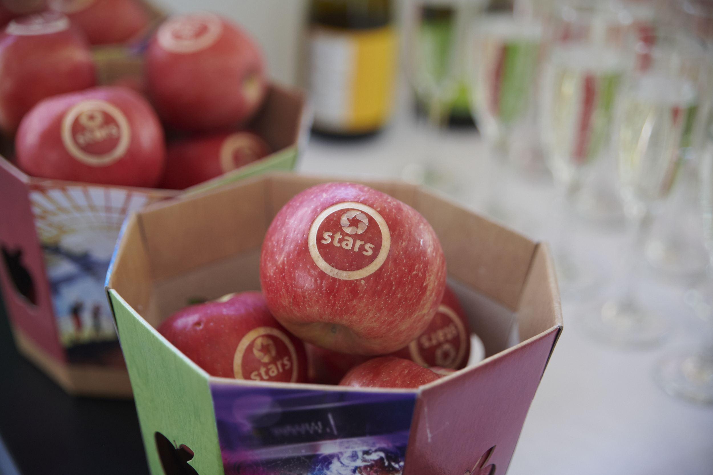 Des pommes rouges décorées, présentées dans des boîtes colorées, symbolisant un événement convivial et festif.