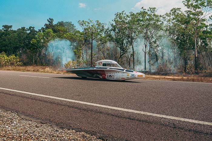 Véhicule innovant circulant sur une route bordée d'arbres, illustrant l'ingéniosité en technologies durables.