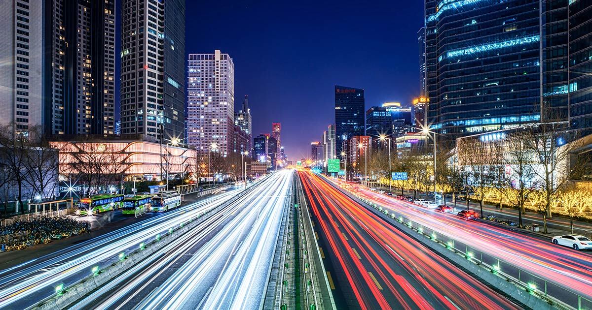 A vibrant cityscape at night, showcasing busy traffic and illuminated skyscrapers, highlighting technological advancement and urban life.