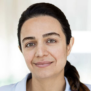 Portrait d'une femme souriante, aux traits marqués, portant une blouse claire, évoquant professionnalisme et bienveillance.