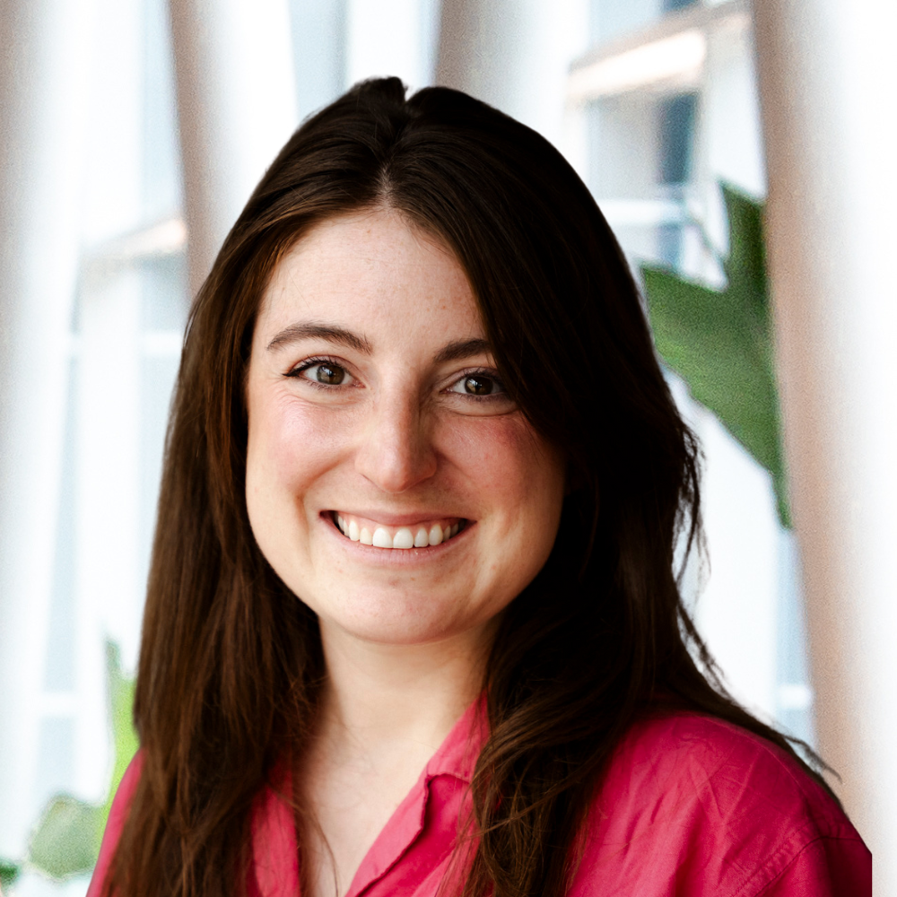 A smiling student in a pink shirt, standing in a modern environment with natural light and greenery, reflecting a vibrant academic atmosphere.