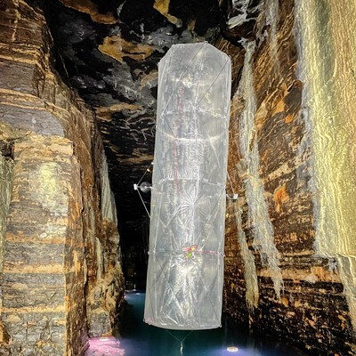 A translucent structure suspended in a cavern, surrounded by textured rock formations and water reflections.