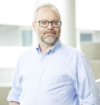 A university professor in a blue shirt, glasses, confident and experienced, standing in a modern building.
