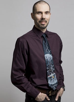 Un professeur en chemise mauve et cravate ornée de motifs, affichant un air professionnel et accueillant.