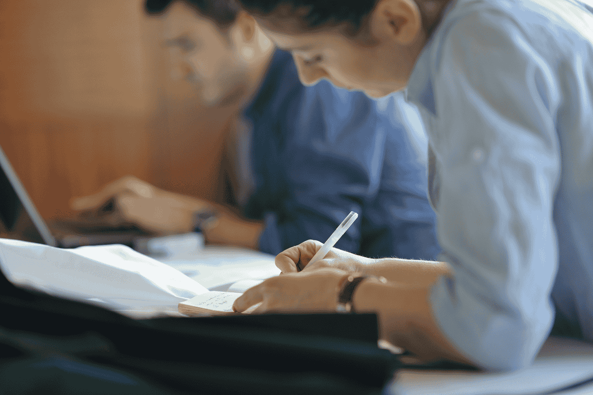 Des étudiants se concentrent sur leurs travaux, l'un écrit des notes tandis que l'autre utilise un ordinateur portable.