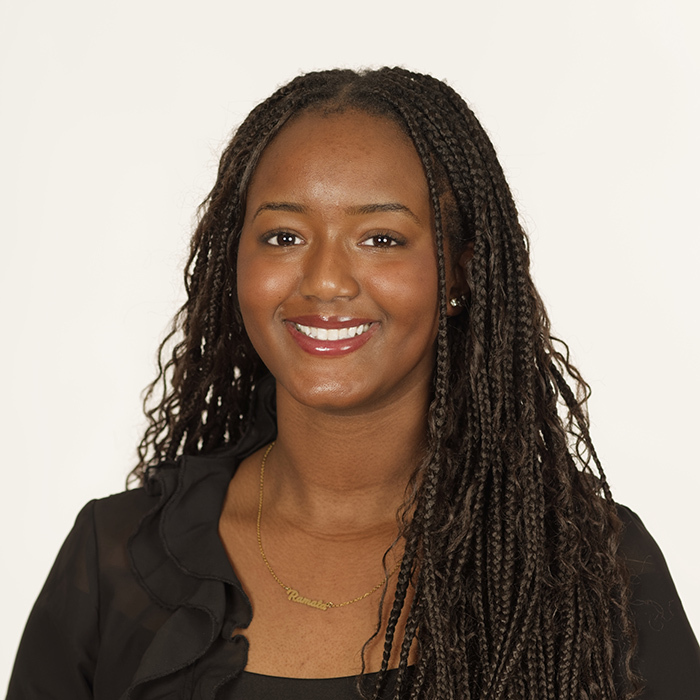 Portrait d'une étudiante souriante, avec des cheveux tressés, portant un haut noir et un collier, symbolisant la réussite universitaire.