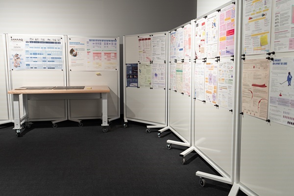 Espace d'exposition dédié aux projets, avec des présentations affichées sur des panneaux mobiles et une table au centre.