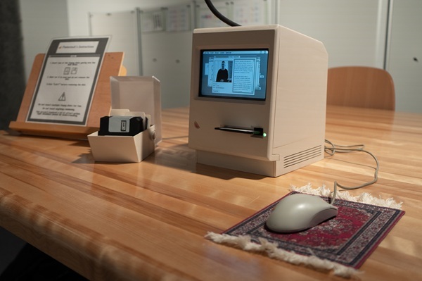 Un ancien ordinateur sur une table en bois, accompagné d'un boîtier de disquettes et d'une souris sur un tapis, évoquant l'innovation technologique.