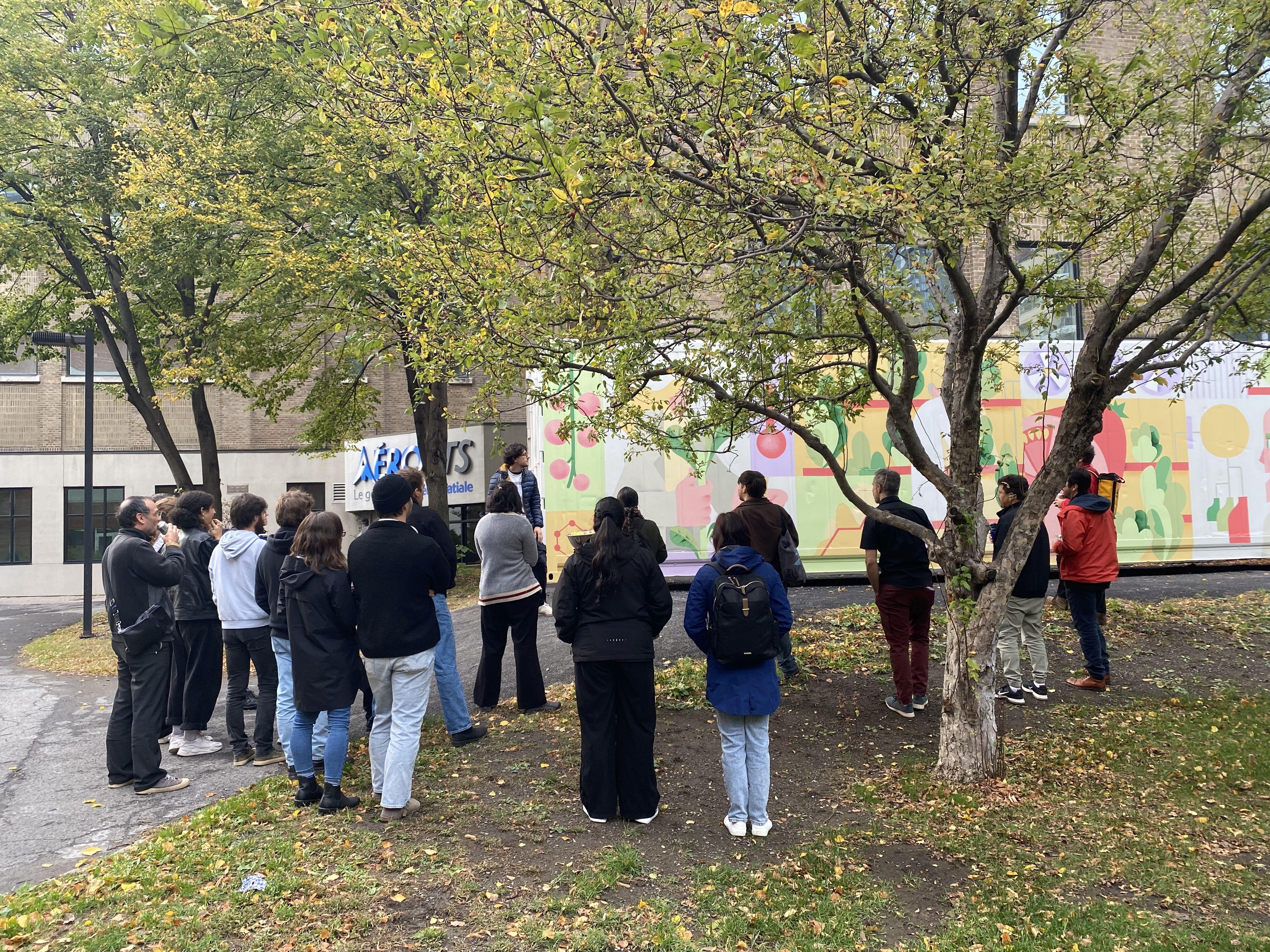 Un groupe d'étudiants observe une activité extérieure, entouré d'arbres, dans une ambiance conviviale et d'apprentissage.