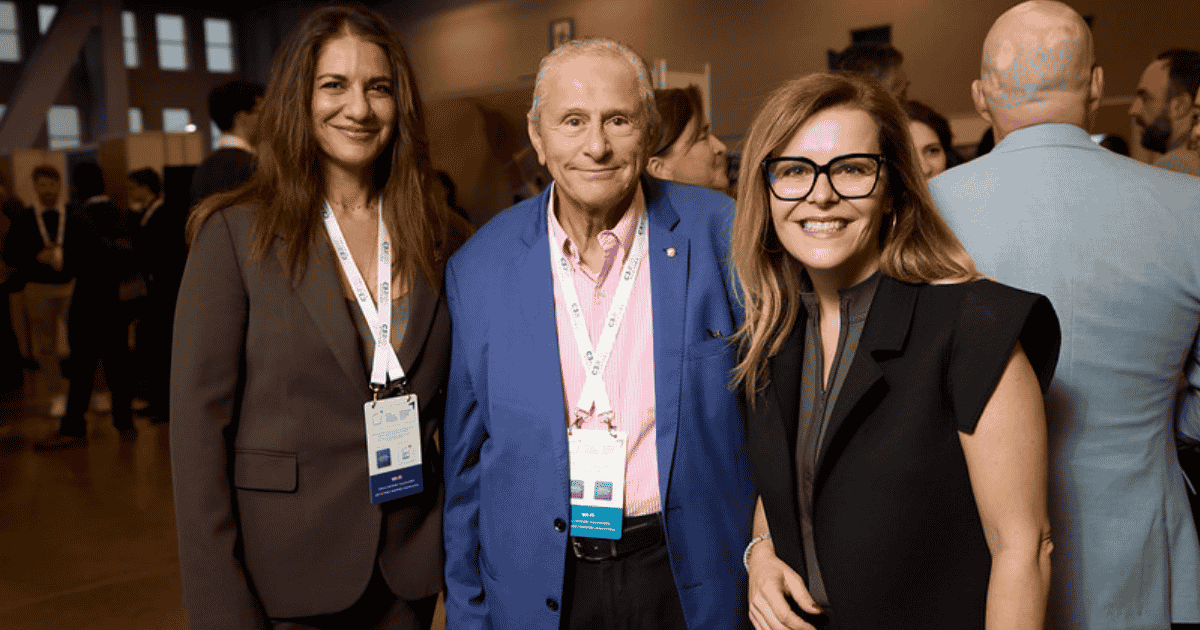 Trois personnes posent ensemble lors d'un événement, souriantes et élégamment habillées, dans une ambiance accueillante et professionnelle.