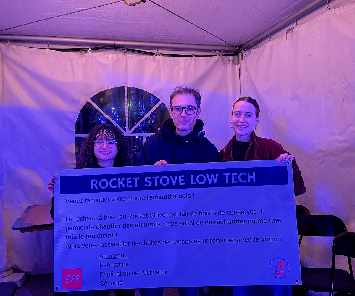 Three people holding a poster under a purple-lit tent.