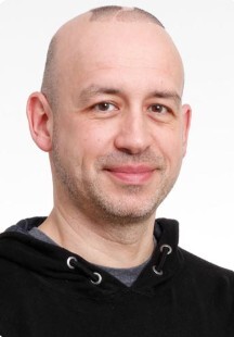 Portrait of a smiling man wearing a black sweater. He displays a warm and welcoming attitude.