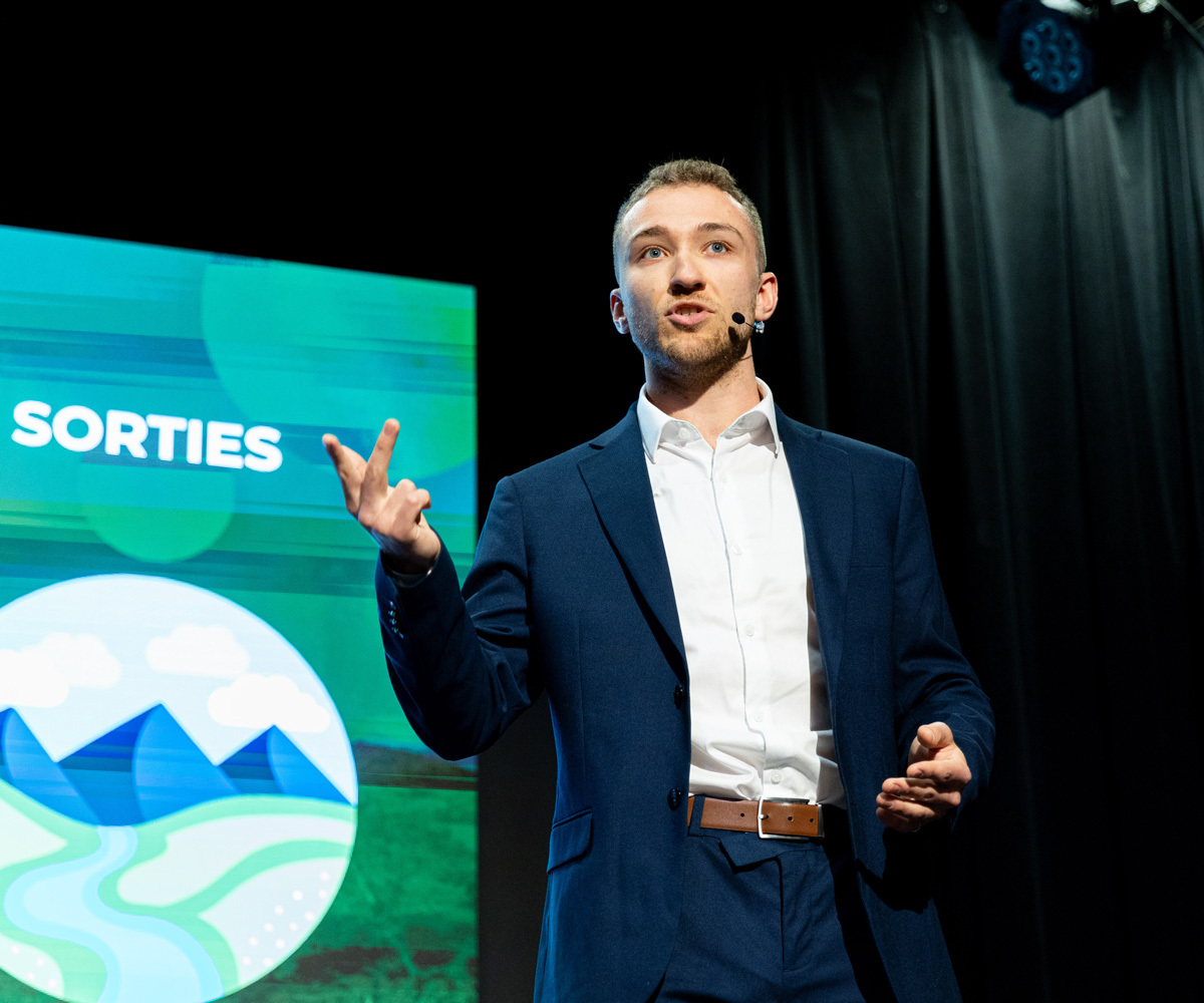 Un étudiant en costume présente des idées, captivant l'audience avec passion et dynamisme lors d'un événement académique.