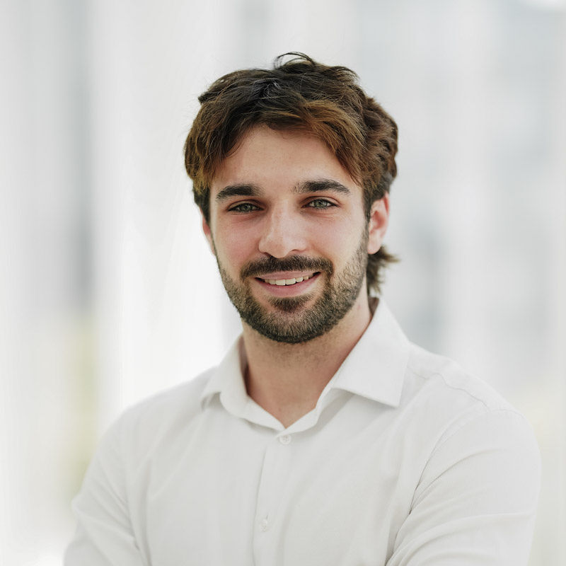 Étudiant souriant en chemise blanche, représentant la dynamique et l'engagement de la communauté universitaire en technologie supérieure.