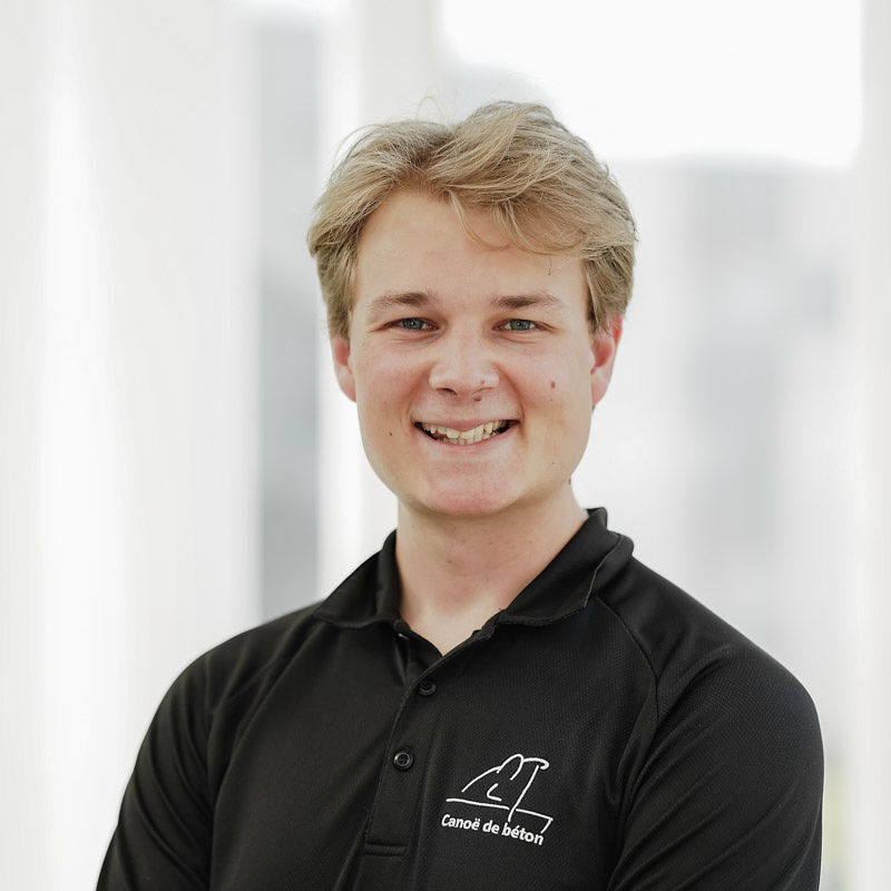 Un étudiant souriant porte un polo noir avec un logo. Il se tient dans un environnement lumineux et professionnel.