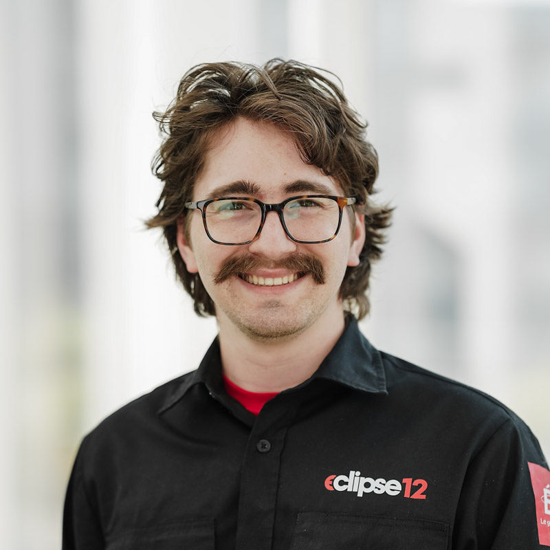 Étudiant souriant en tenue de travail, affiche une attitude chaleureuse et professionnelle. Parfait pour un environnement technologique.