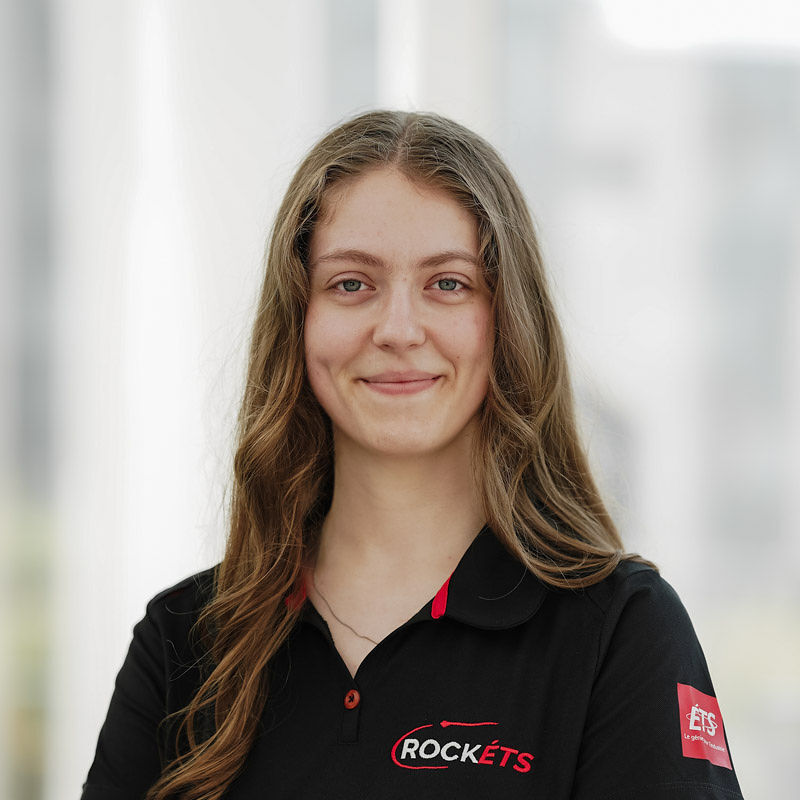 Étudiante enthousiaste en ingénierie, membre de l'équipe ROCKETS, portant un polo noir, souriante et prête à relever des défis.