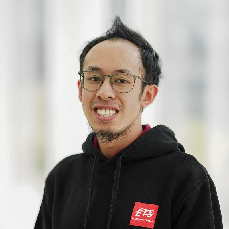 Étudiant souriant portant un hoodie noir, prêt à relever des défis en ingénierie à l'ÉTS. Ambiance dynamique et inspirante.