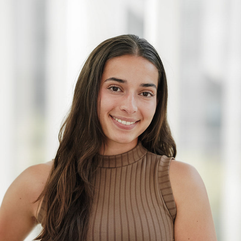 Personne souriante en tenue moderne, se tenant dans un environnement lumineux et contemporain, reflétant confiance et engagement.