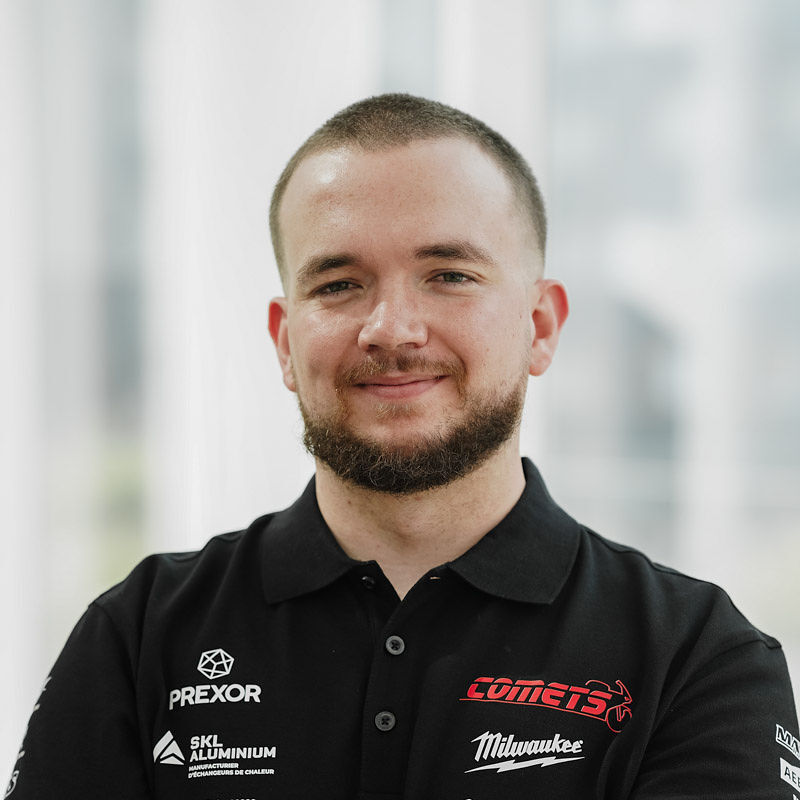 Étudiant souriant en polo noir, représentant des sponsors, dans un environnement lumineux et moderne, comme celui d'une université technologique.