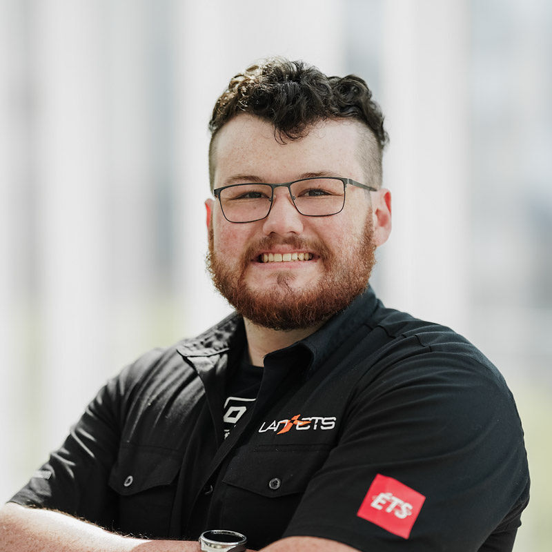 Étudiant souriant, portant des lunettes et un uniforme noir, il incarne l'esprit dynamique et innovant de l'Université en technologie supérieure.