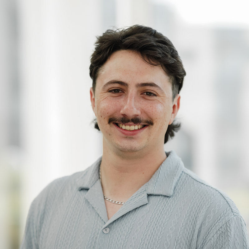 Étudiant souriant en chemise légère, il incarne la créativité et l'enthousiasme propres à l'Université en technologie supérieure.