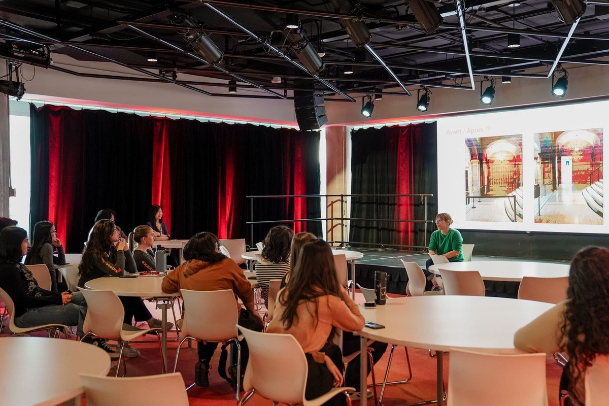 Séance interactive dans un espace moderne, avec des étudiants attentifs écoutant une présentatrice devant un écran de projet.