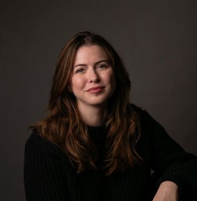 Étudiante fière, souriante, vêtue d'un pull noir, incarnant la passion et la détermination au sein d'un environnement technologique.