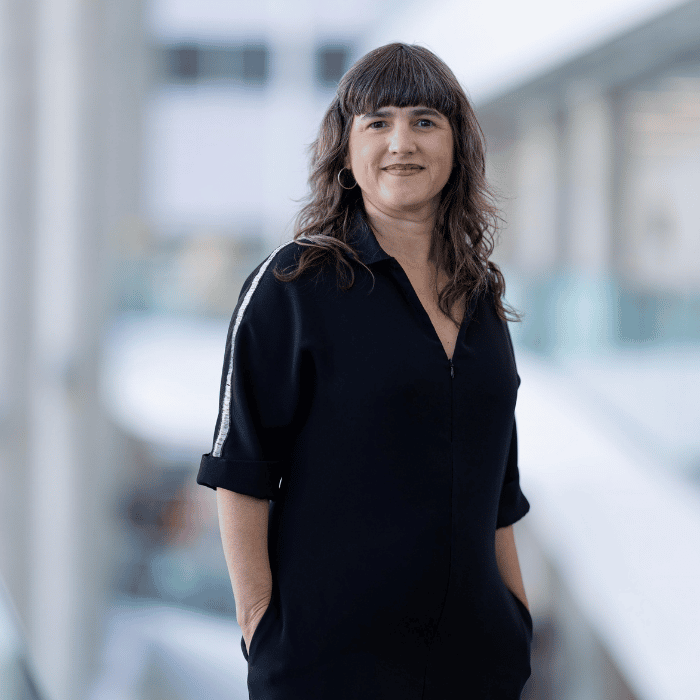 Portrait d'une femme souriante, vêtue d'une tenue noire élégante, se tenant dans un environnement moderne et lumineux, promouvant l'innovation.