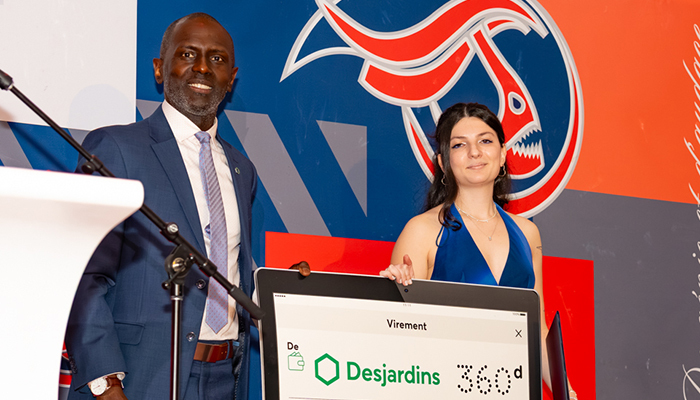 Célébration d'une remise de prix, avec une étudiante et un intervenant posant fièrement devant un décor coloré de l’institution.