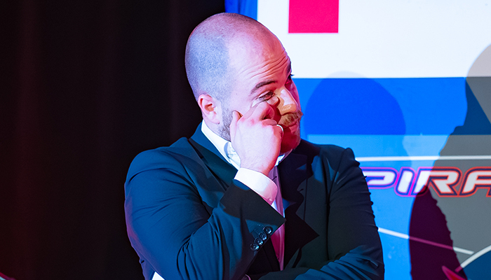Un homme en costume exprime des émotions tout en réfléchissant, sous un éclairage coloré. Ambiance intense et captivante.