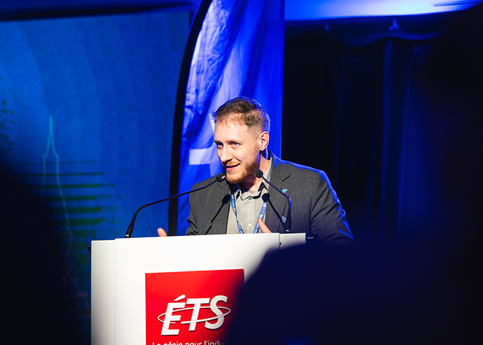 Un intervenant dynamique s'adresse à un public lors d'un événement à l'ÉTS, illustrant l'importance de l'innovation technologique.