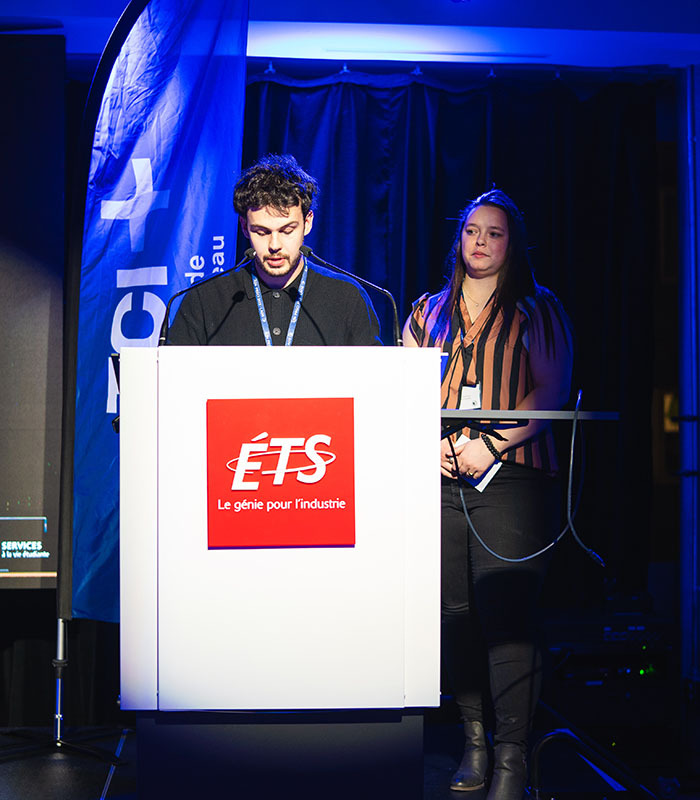 Deux étudiants présentent devant un auditoire lors d'un événement à l'ÉTS, symbolisant l'innovation et l'engagement académique.