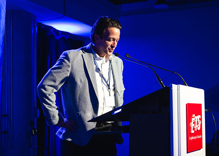 Un intervenant s'apprête à prendre la parole sur scène lors d'un événement à l'ÉTS, sous un éclairage captivant.