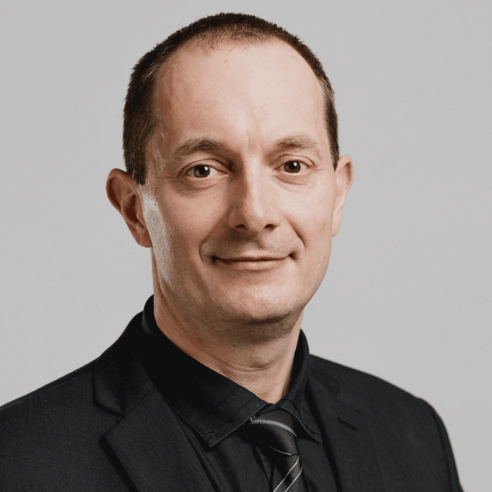 Professeur en technologie, il affiche une allure professionnelle avec un sourire confiant dans un costume noir.
