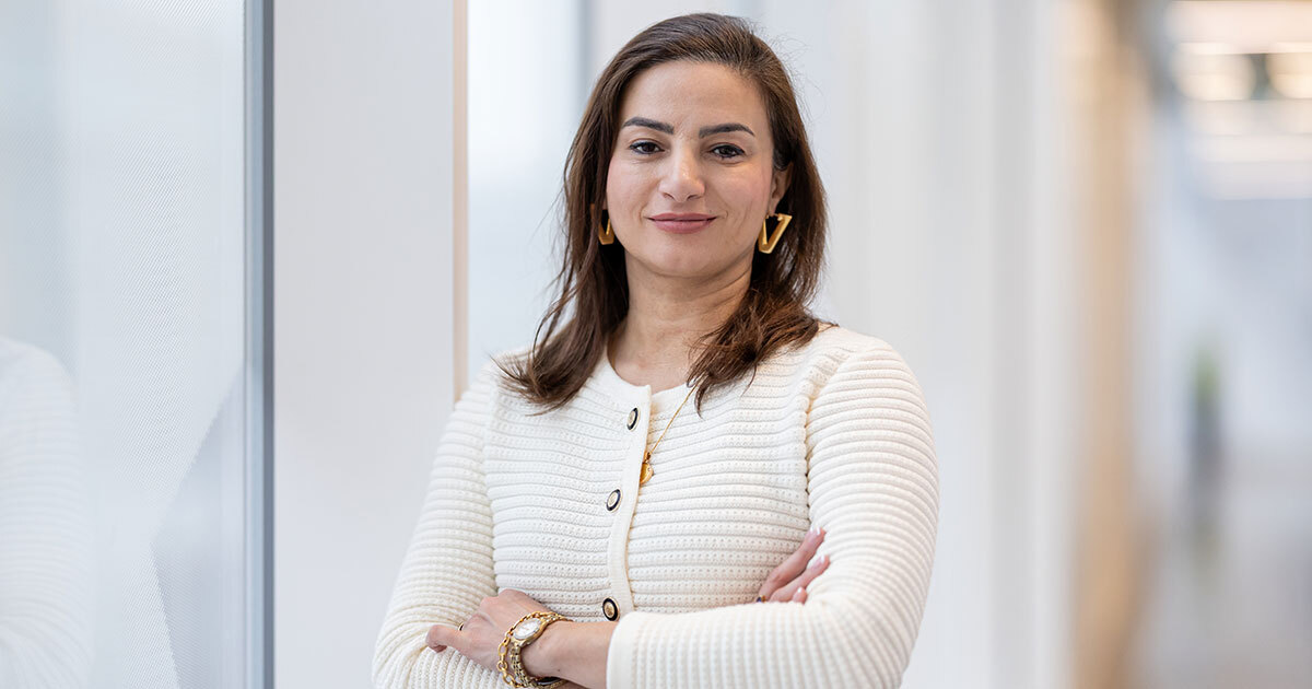 Confident woman in a white jacket, arms crossed, standing in a modern and bright environment. Positive energy and determination.