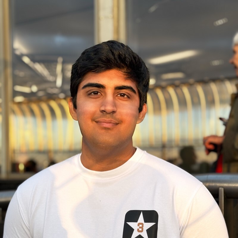 Étudiant souriant, portant un t-shirt blanc, dans une ambiance lumineuse et moderne, entouré d'une architecture contemporaine.