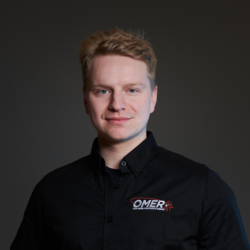 Étudiant en technologie, il porte une chemise noire avec le logo OMER, affichant un sourire confiant dans un cadre sobre.