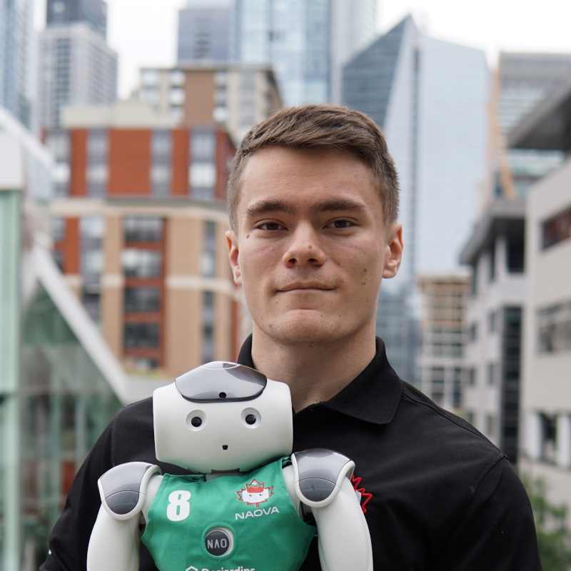 Un étudiant en technologie supérieure pose fièrement avec un petit robot, symbole d'innovation et de recherche en robotique.