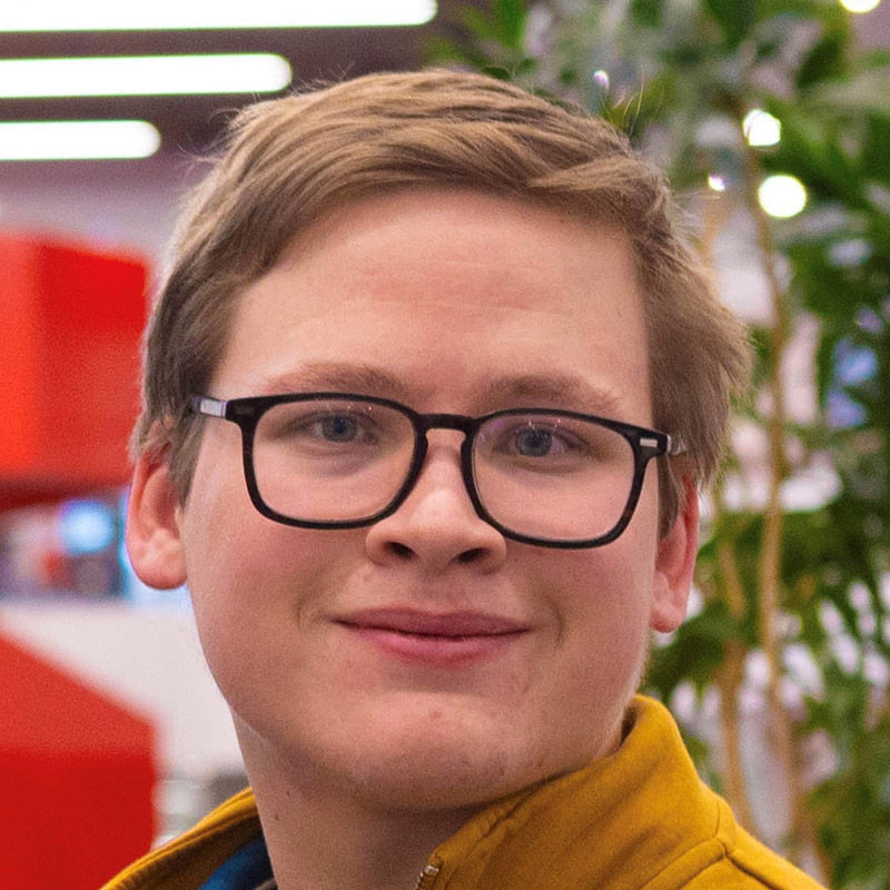 Un étudiant souriant se tient devant un environnement moderne, avec des touches de verdure et un éclairage contemporain.