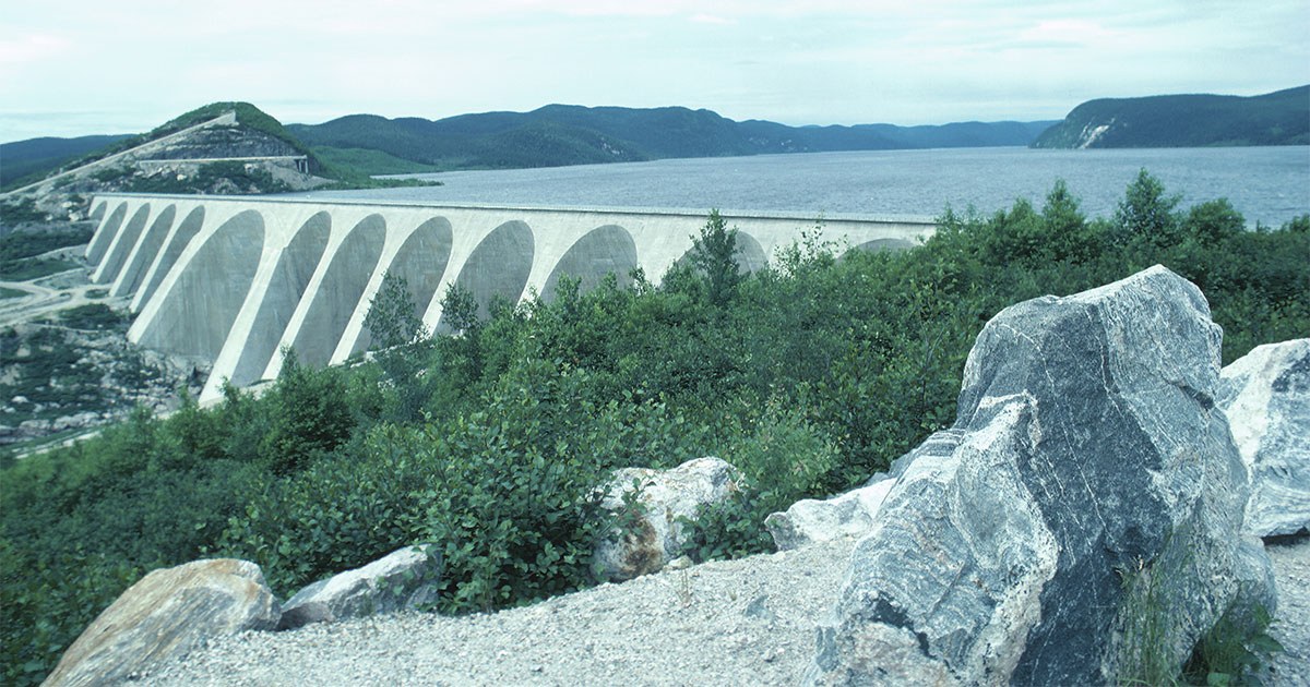 Un panorama impressionnant d'un barrage se déployant majestueusement au bord d'un lac, entouré de montagnes verdoyantes.