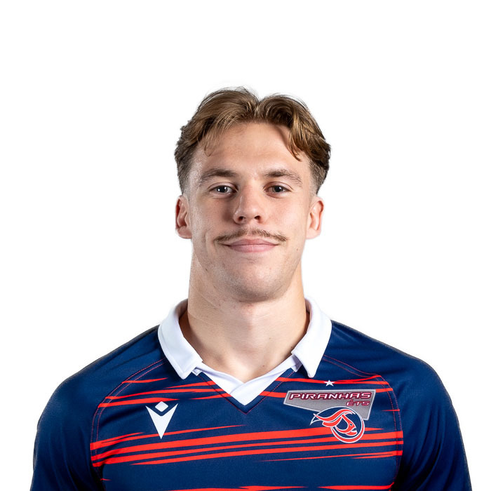 Un jeune homme souriant porte un maillot aux couleurs vives, représentant une équipe sportive, avec un fond neutre.
