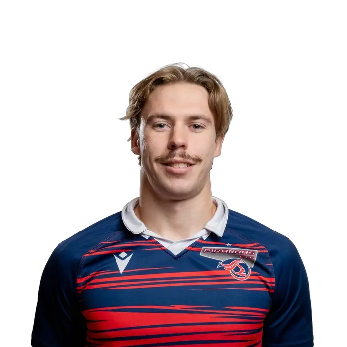 Un jeune homme souriant porte un maillot aux couleurs vives, représentant une équipe sportive, avec un fond neutre.
