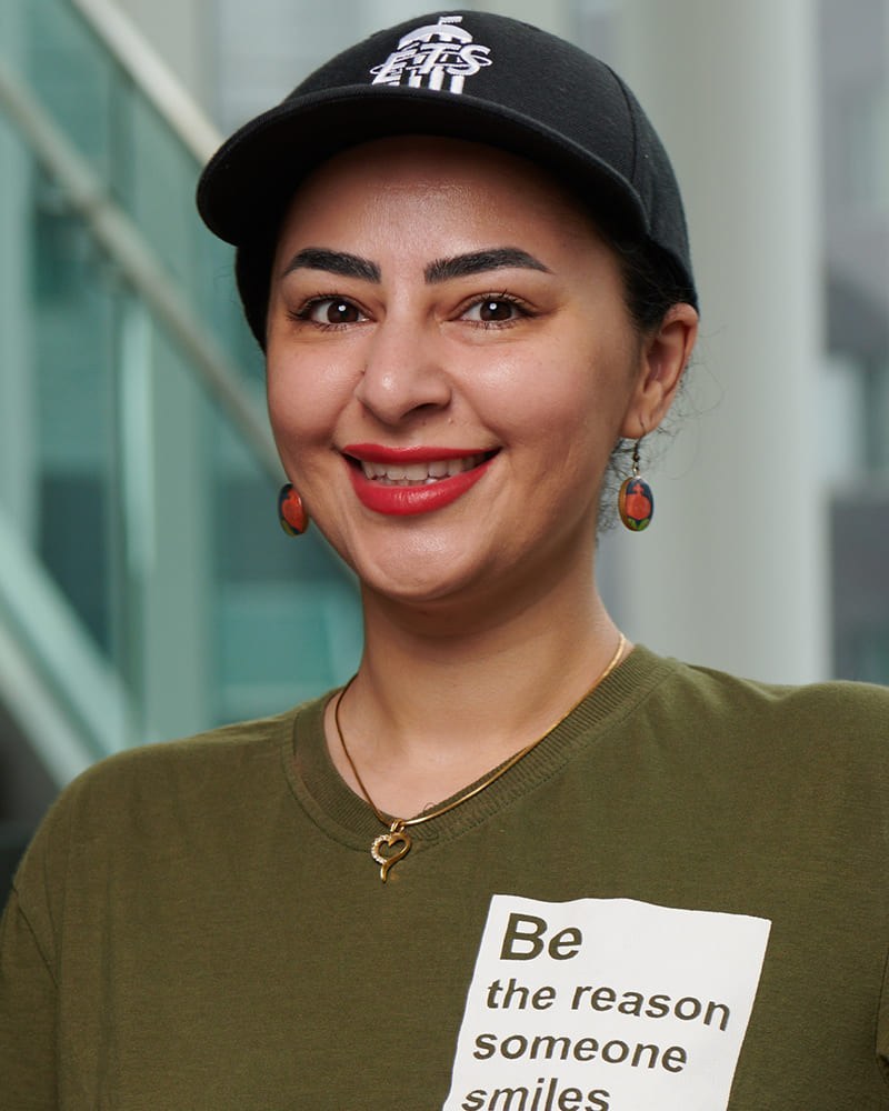 Une étudiante souriante porte un t-shirt portant un message positif et une casquette, affichant confiance et convivialité.