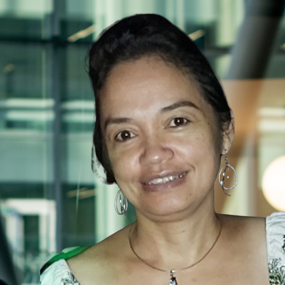 A smiling individual in a casual outfit, set against a modern, glass-windowed background, exuding warmth and approachability.