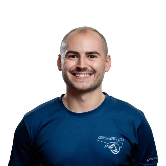 Étudiant souriant en t-shirt rouge, prêt à relever de nouveaux défis en technologie. Ambiance dynamique et conviviale.