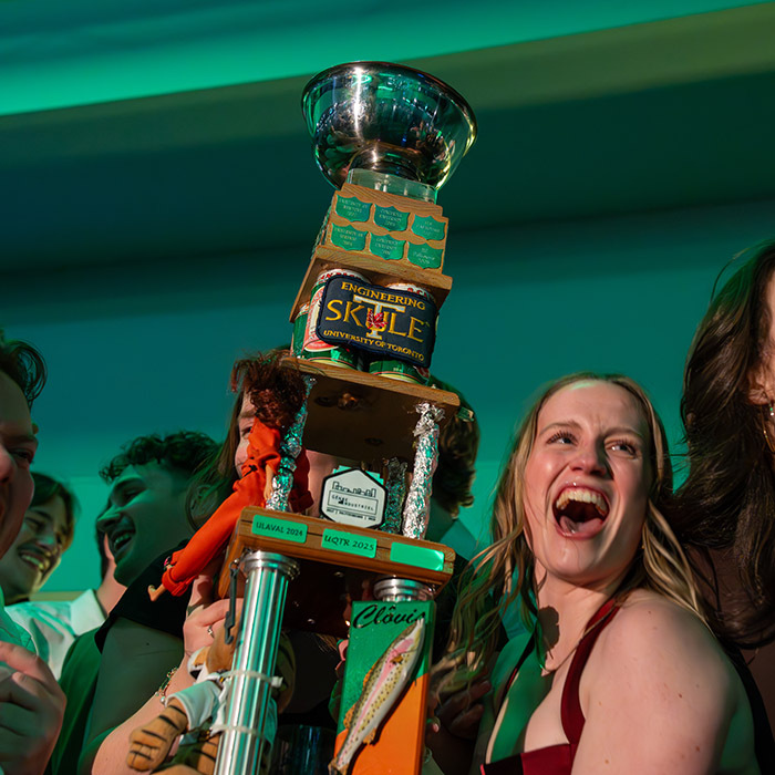 Celebrating a victory with a unique trophy, surrounded by joyful students at an engineering event.