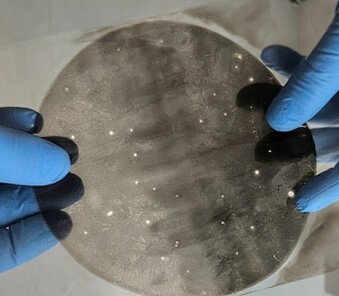 Un disque transparent avec des motifs lumineux, manipulé avec des gants, suggérant une recherche en science ou en technologie avancée.
